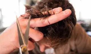 Mains d'une coiffeuse coupant une mèche de cheveux aux ciseaux